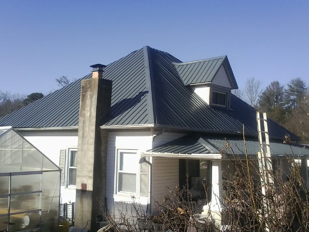 Dark blue standing seam metal roof on a white farmhouse with dormer — Slate & Tile Roof Repair by Roofing Brothers in Sand Creek