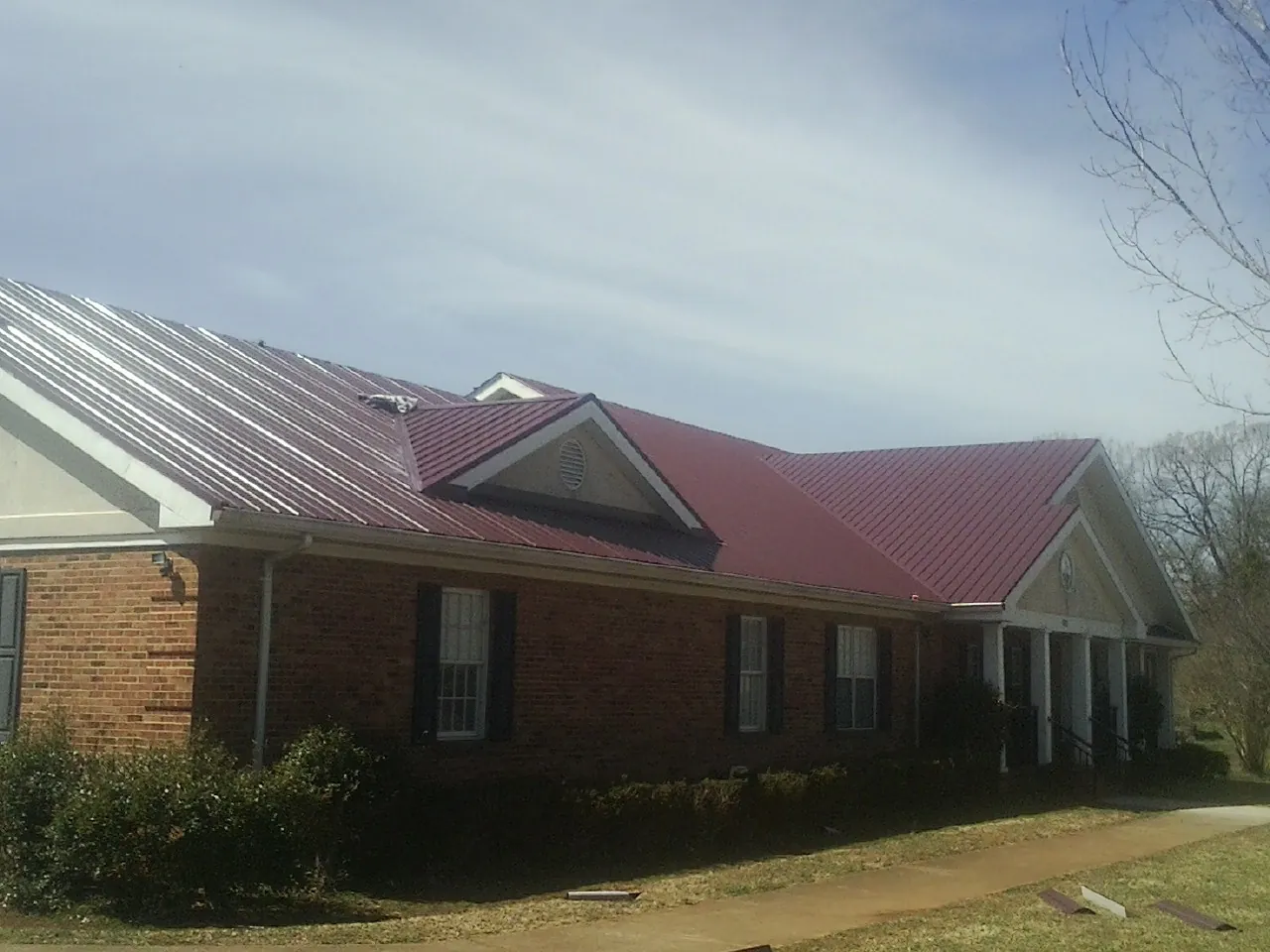 Red metal roof with gabled entries on a long brick building, from a Hail Damage Roof Repair job in Sand Creek