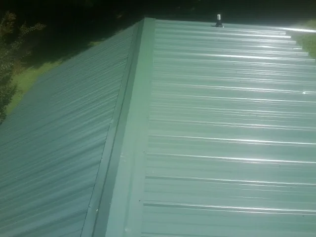 New green metal panels meeting at the ridge of a roof — Flat Roof Repair work by our crew in Sand Creek
