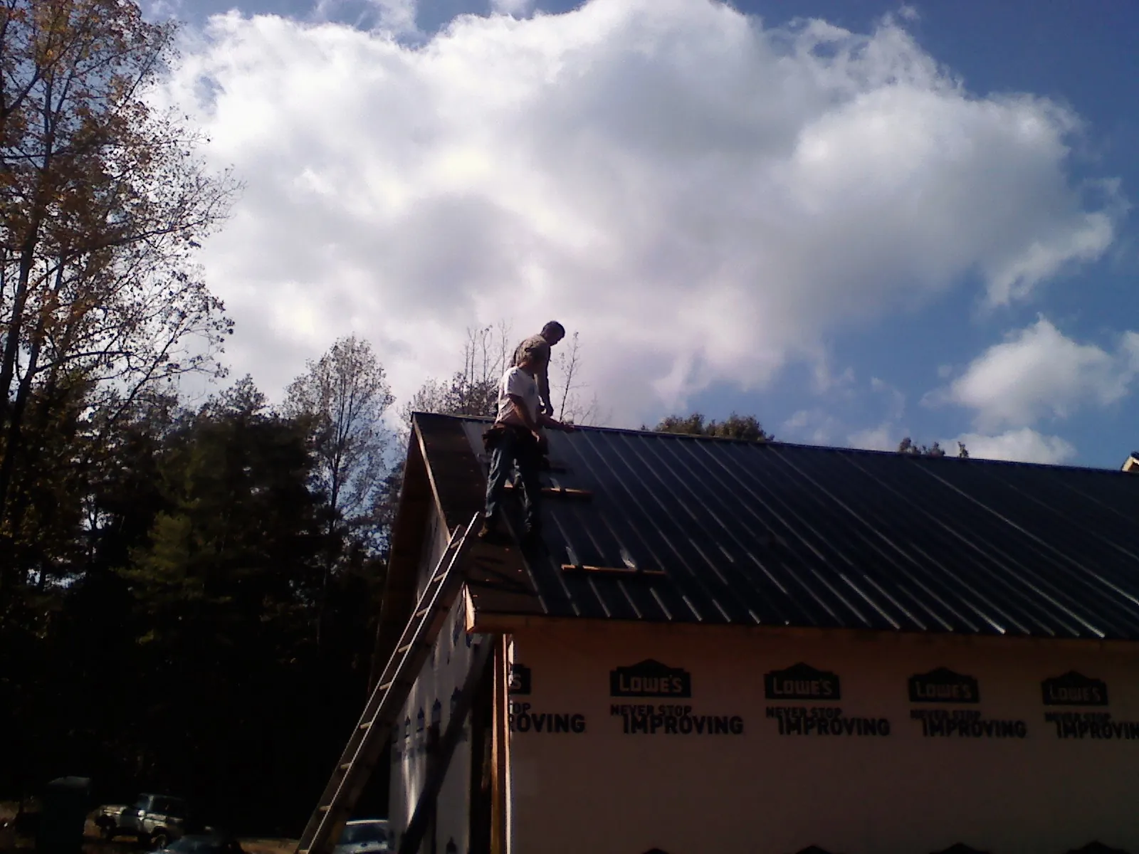 Roofer fastening dark metal panels high against a cloudy sky, from a Roof Inspection job in Sand Creek