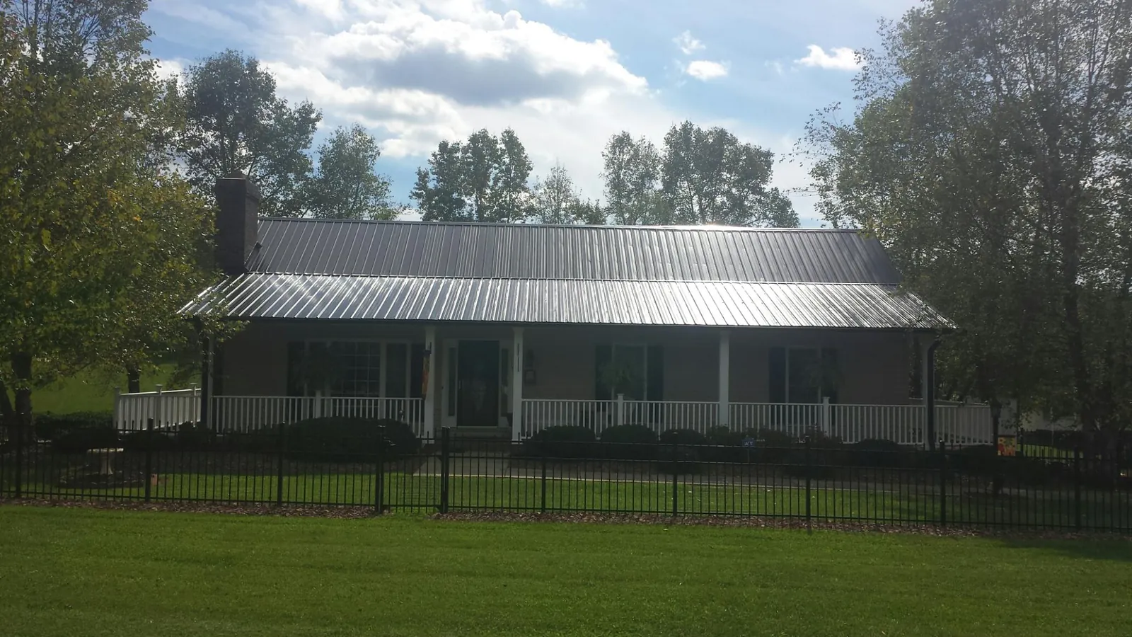 Gray metal roof on a brick ranch with a full width front porch — Gutter Guard Installation work by our crew in Sand Creek