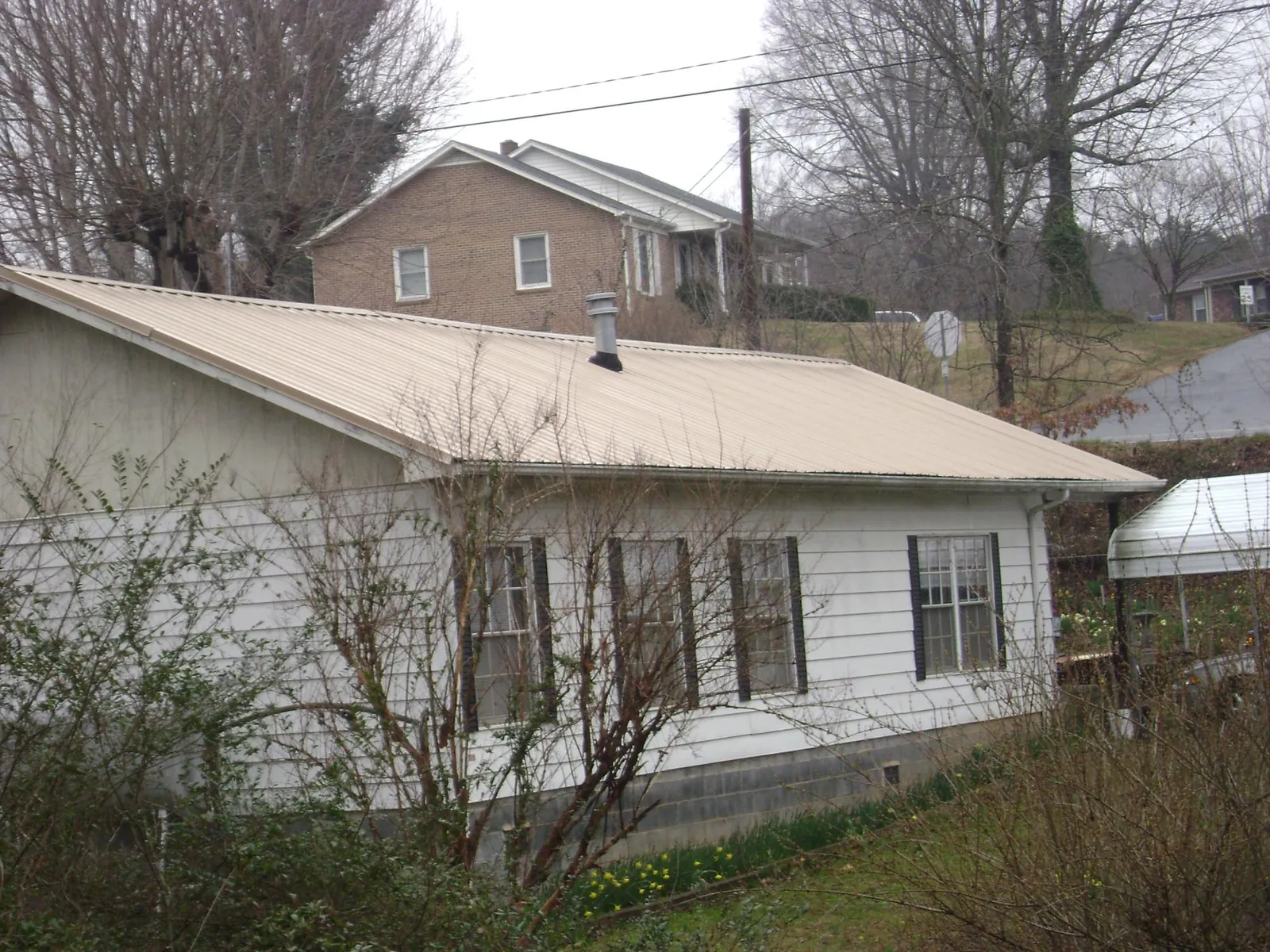 Tan metal roof on a white sided house set into a hillside — Commercial Roofing by Roofing Brothers in Sand Creek