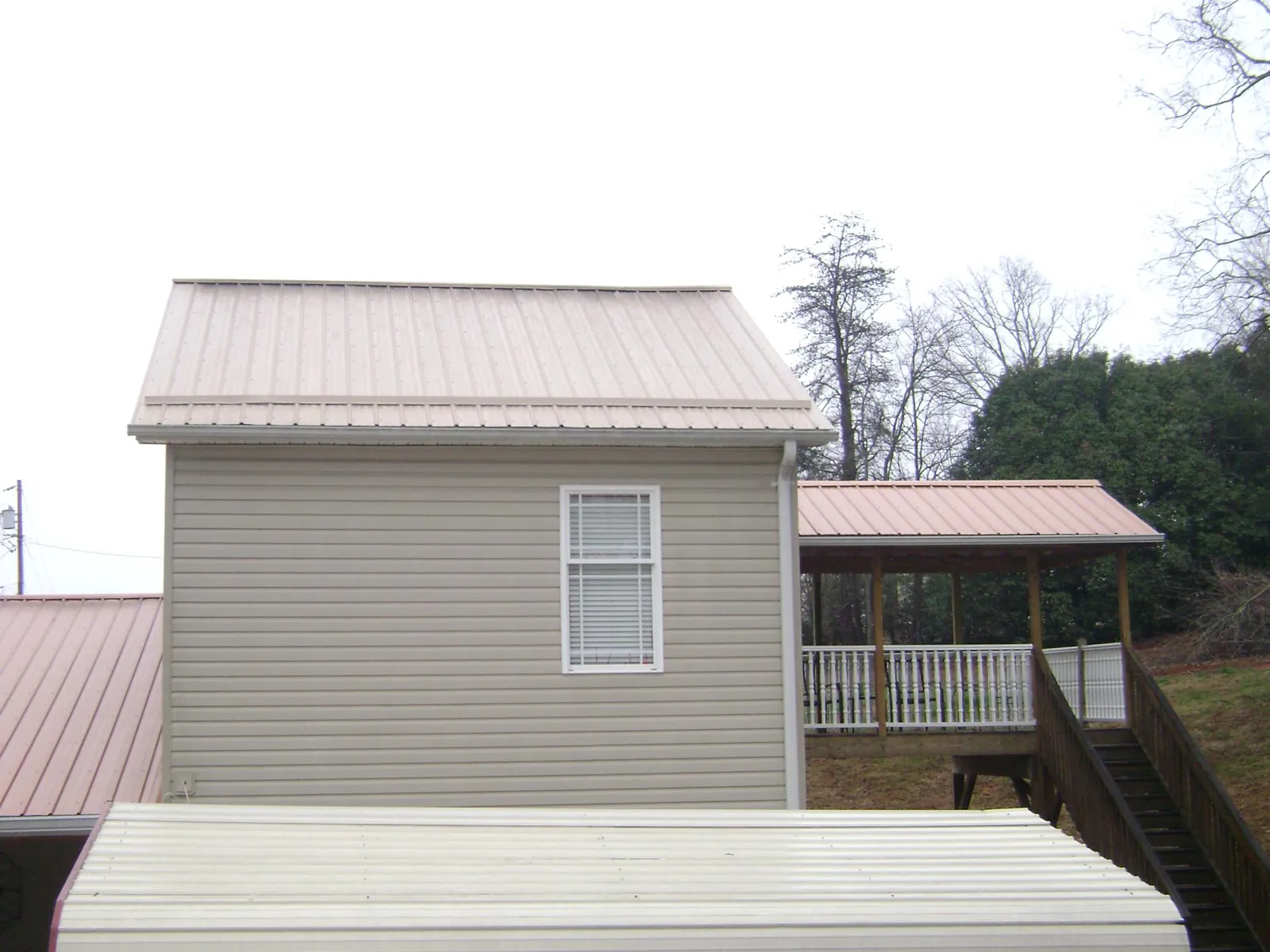 Tan metal roofs on a two story addition and attached porch, from a Roof Replacement job in Sand Creek